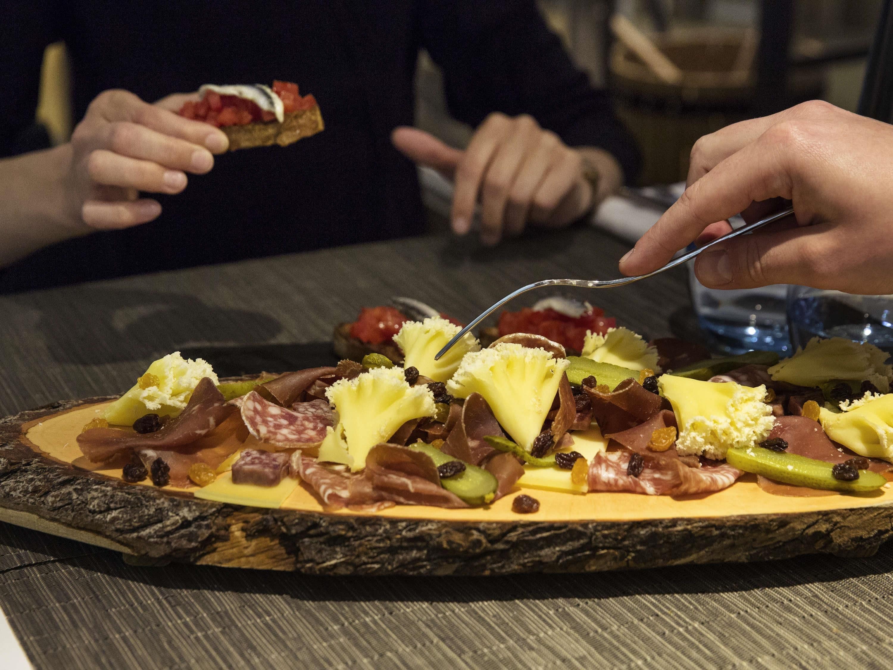 Une planche de service en bois, sur laquelle sont disposés divers aliments, notamment du fromage, de la charcuterie et des légumes.