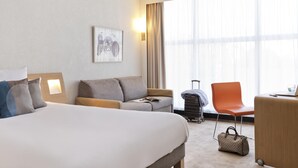 A hotel room with a bed, a sofa, a desk, a chair, a suitcase, and a handbag.