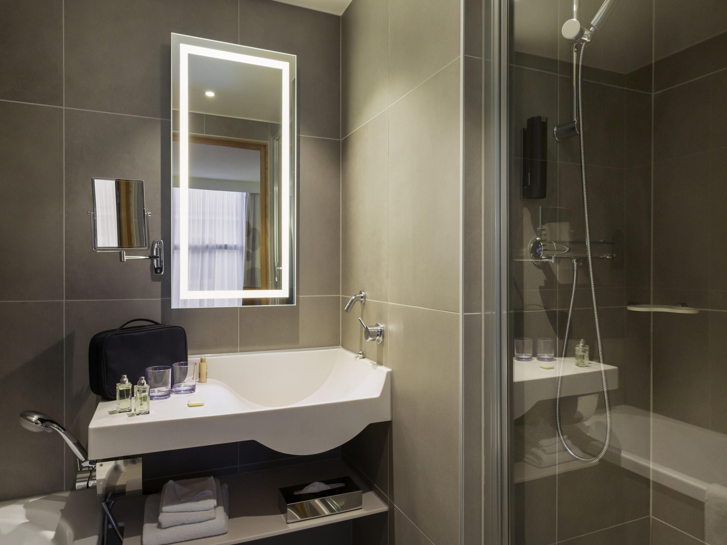 Een moderne badkamer met een grote spiegel, een witte wastafel, een douche en een douchecabine met glazen wanden.