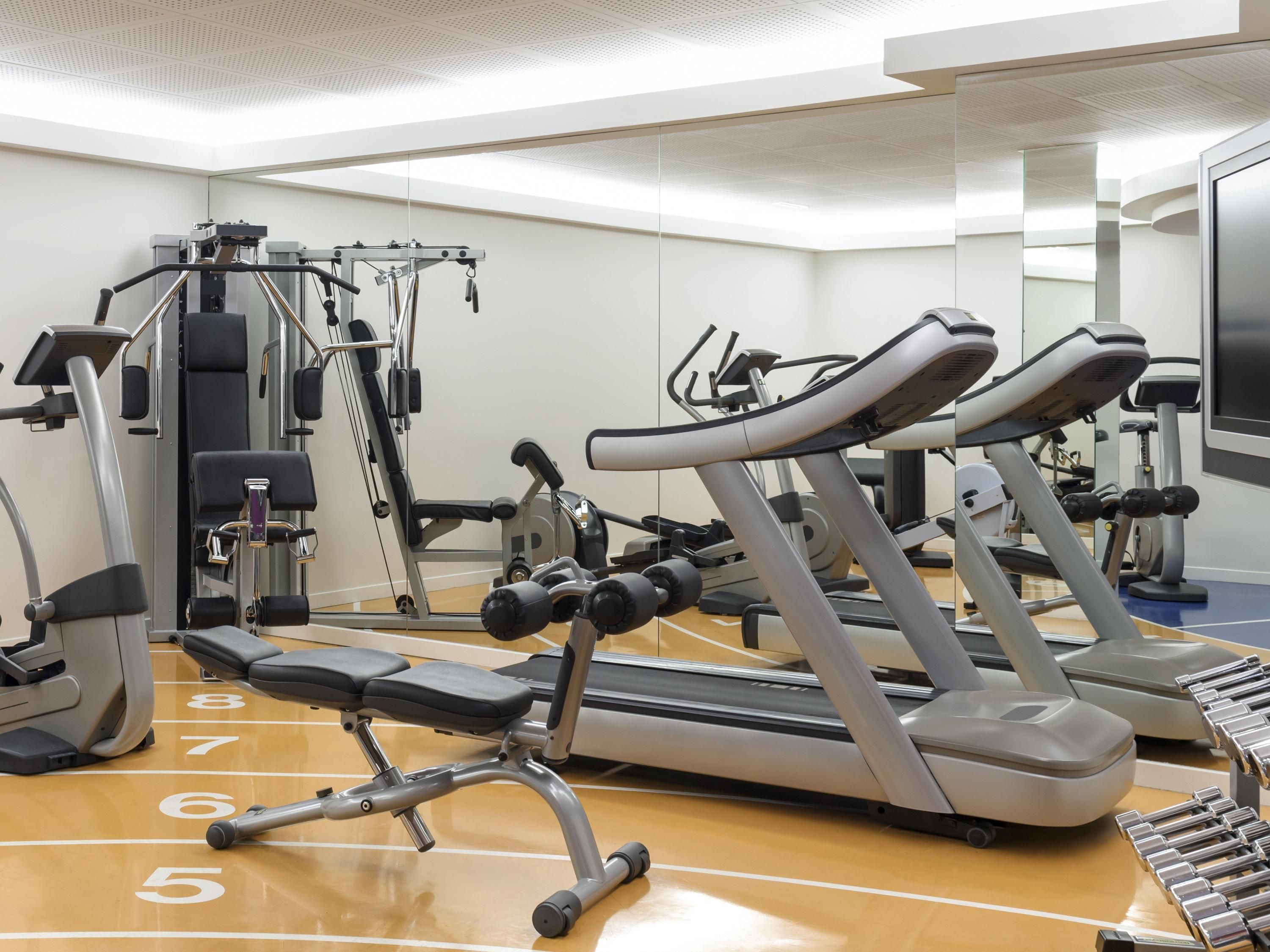A gym with exercise equipment, a mirrored wall, and a wooden floor with numbered steps.