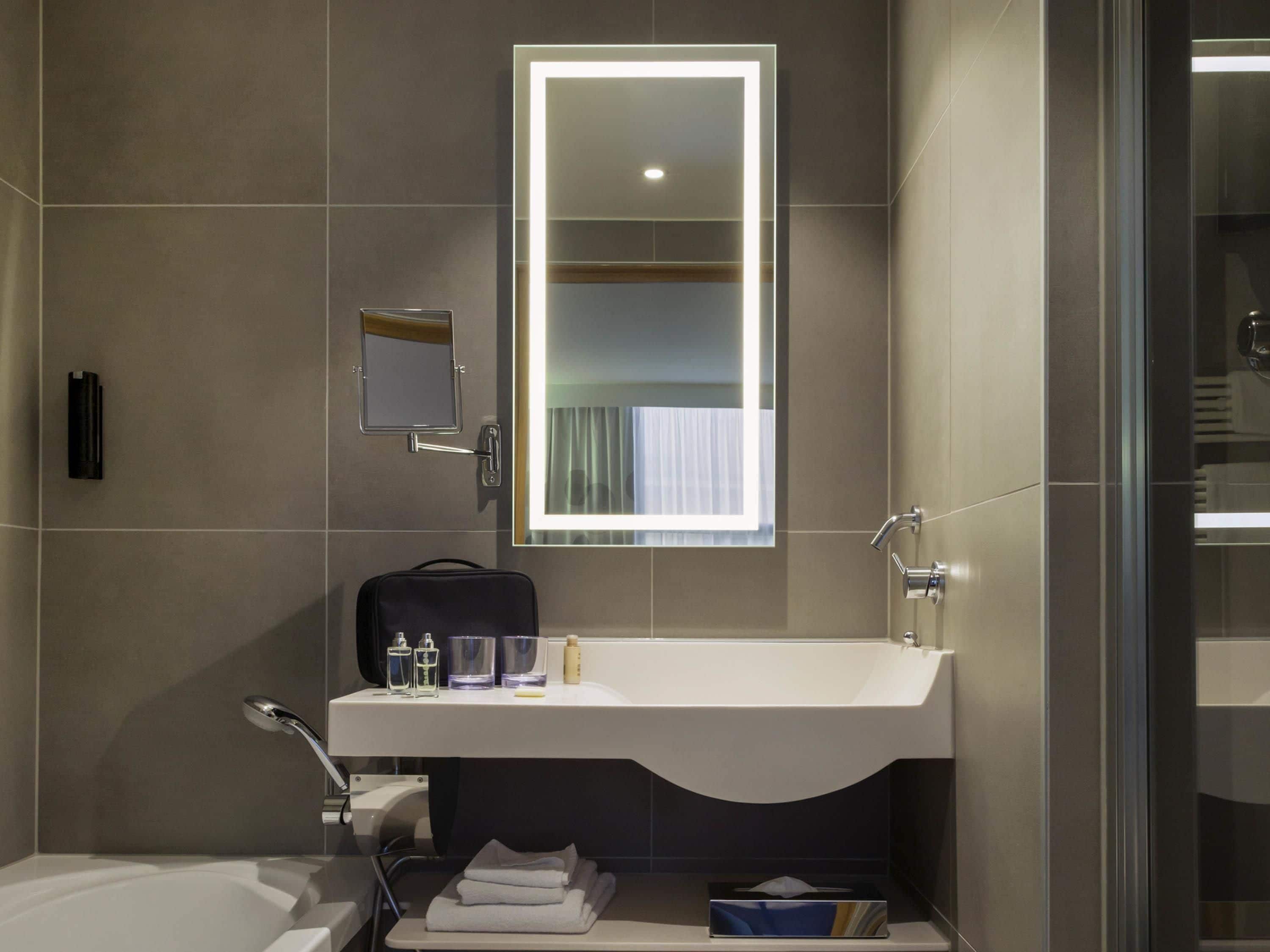 A modern bathroom with a white sink, a mirror, a towel rack, and a glass shower enclosure.