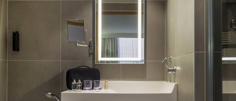 A modern bathroom with a white sink, a mirror, a towel rack, and a glass shower enclosure.