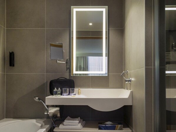 Un baño moderno con un lavamanos blanco, un espejo, un perchero para toallas y un box de ducha de vidrio.