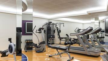 Un gimnasio con cintas de correr, máquinas de pesas y un espejo grande.