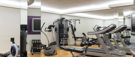 A gym with treadmills, weight machines, and a mirrored wall.