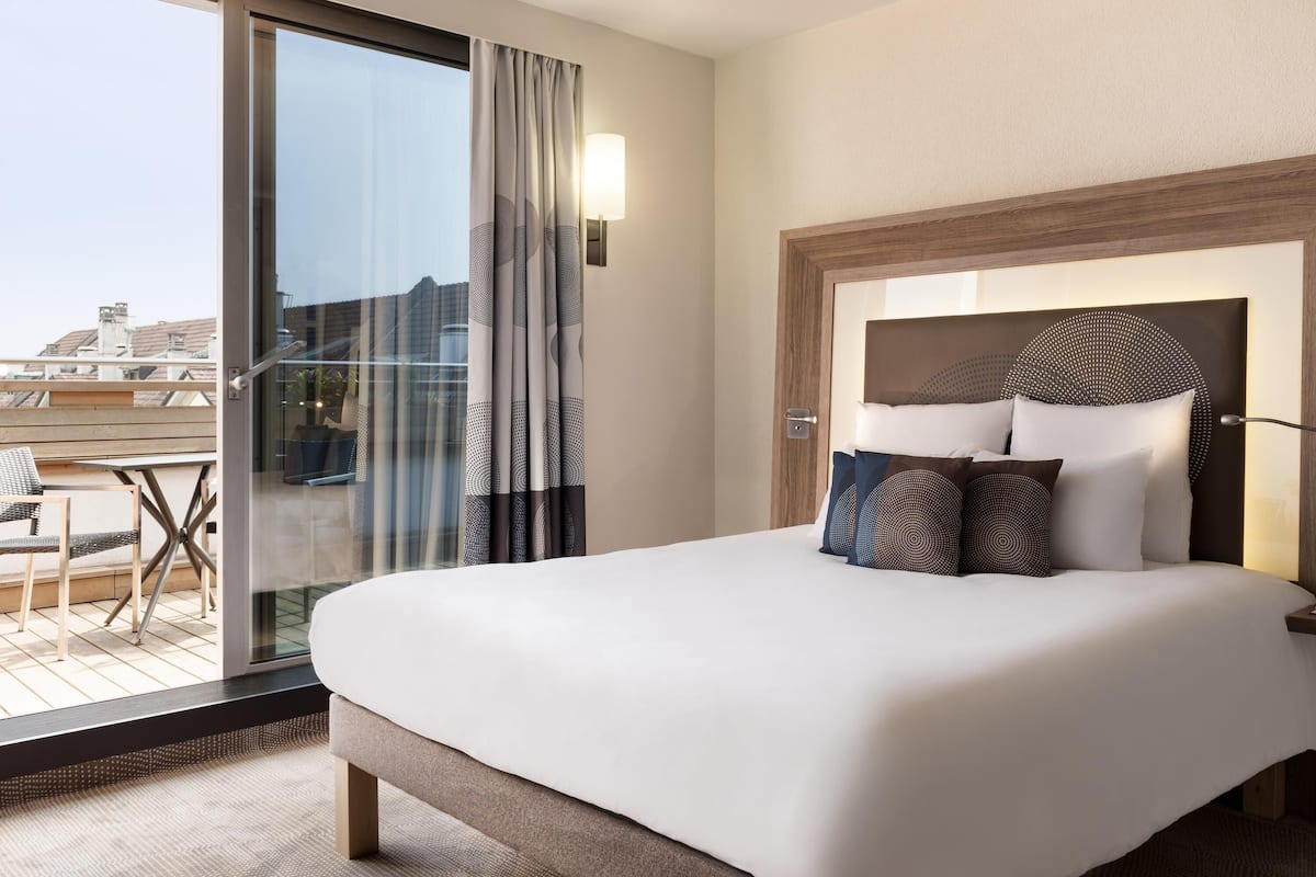 Ett hotellrum med en stor säng, en glasdörr som leder ut till en balkong och en modern sänggavel.