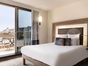 Una habitación de hotel con una cama grande, un puerta de vidrio que da a un balcón y un cabecero moderno.