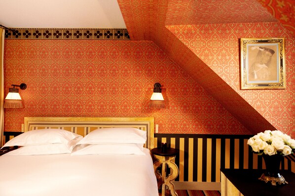 A hotel room with a bed, two wall-mounted lamps, a nightstand, a small table with a vase of flowers, and a framed picture on the wall.