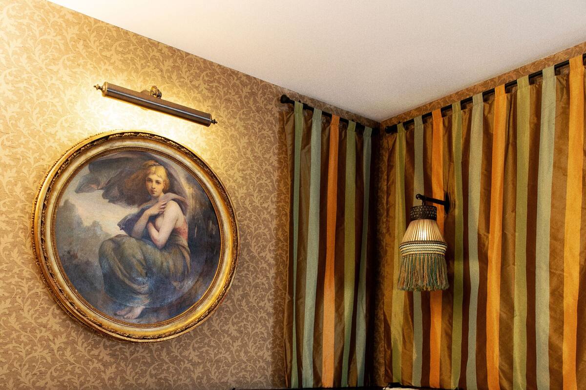 A hotel room with a bed, a framed painting on the wall, and a hanging lamp.