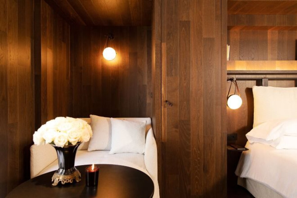 Una habitación acogedora con techo de madera, una mesa redonda con un jarrón de flores blancas y una cama con ropa de cama blanca.