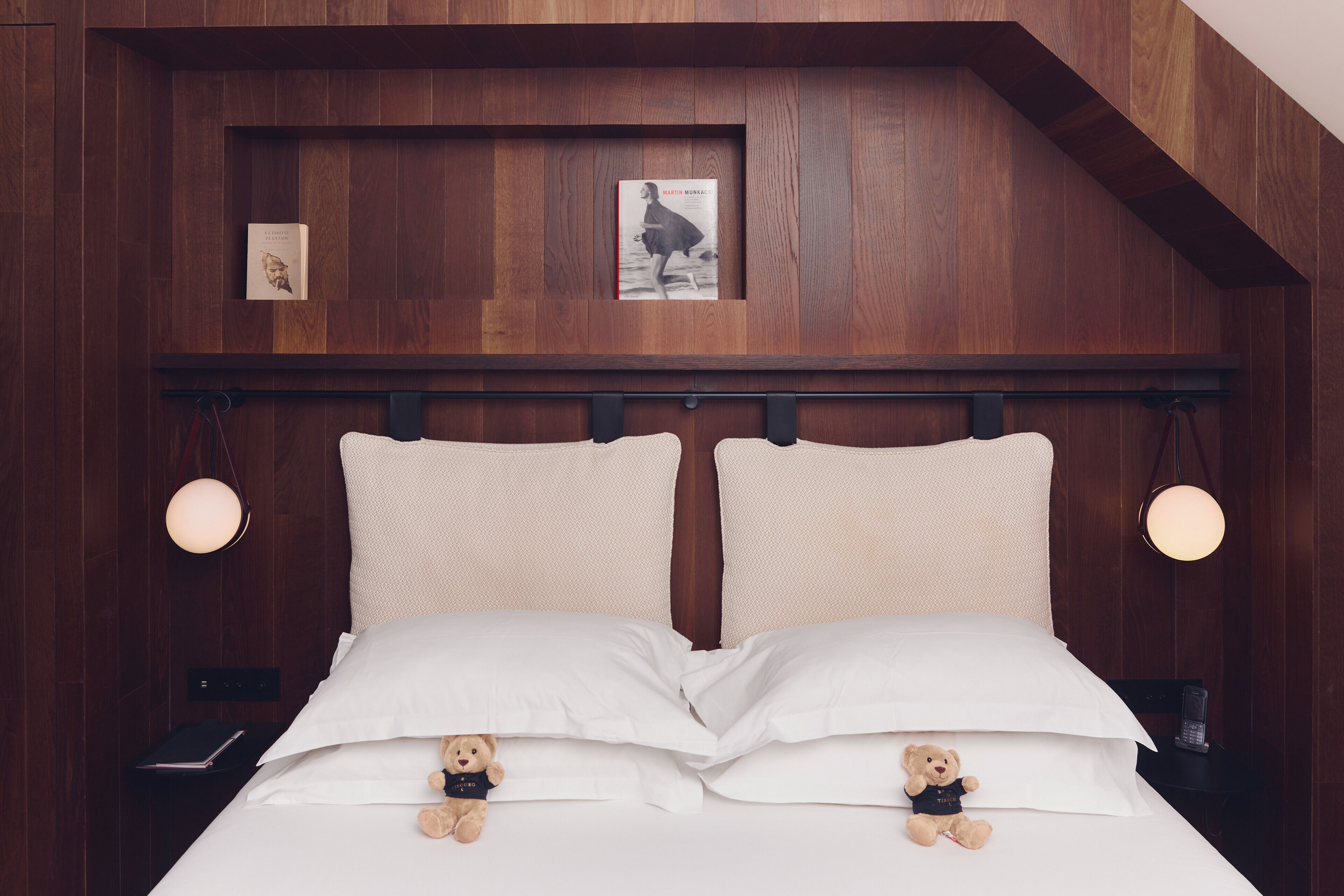 A bed with two pillows, a headboard with a shelf, and two bedside tables with lamps.