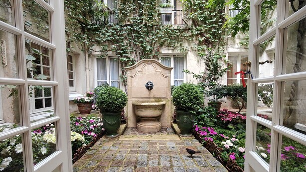 Une cour intérieure avec une fontaine centrale, entourée de plantes et de fleurs en pot.