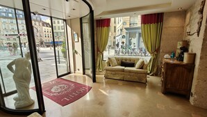 Un hall d’hôtel avec un canapé, une statue et un tapis rouge orné du nom de l’hôtel.