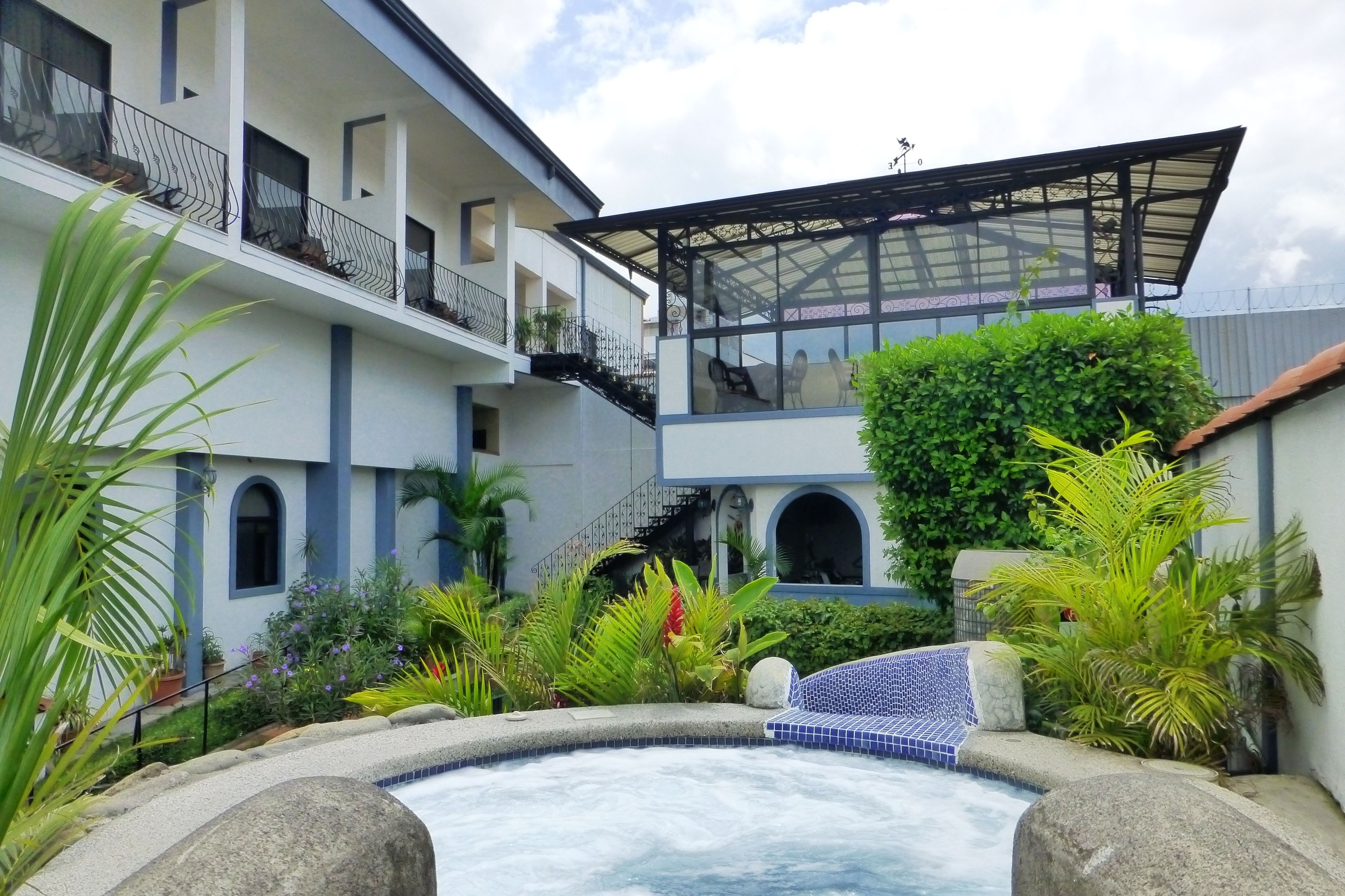 A multi-story building with balconies, a covered outdoor seating area, and a hot tub surrounded by tropical plants.