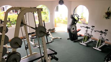 Un gimnasio con varios equipos de ejercicio, incluyendo máquinas de pesas y máquinas de cardio, y ventanas amplias con vistas a zonas verdes.