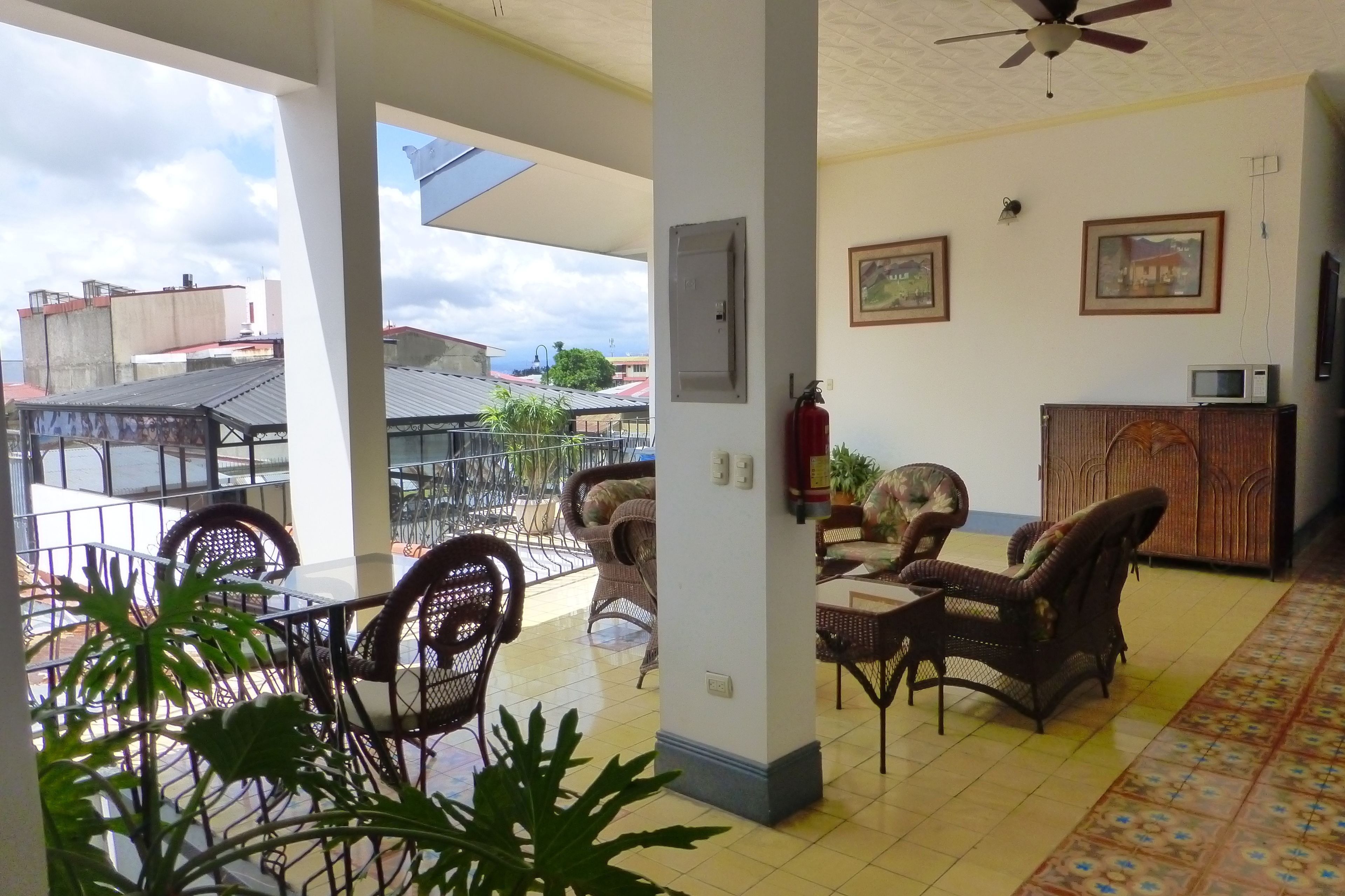 A spacious living area with a balcony, wicker furniture, a television, and a fire extinguisher.