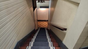 A narrow hallway with a patterned carpet, a wooden railing, and a door at the end.