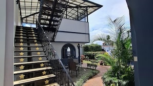 A staircase with decorative elements, a covered outdoor area with plants, and a building with a white facade.
