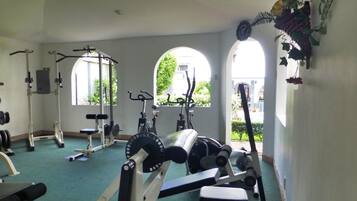 Un gimnasio con diversos equipos de ejercicio, ventanas amplias y vistas al exterior con zonas verdes.