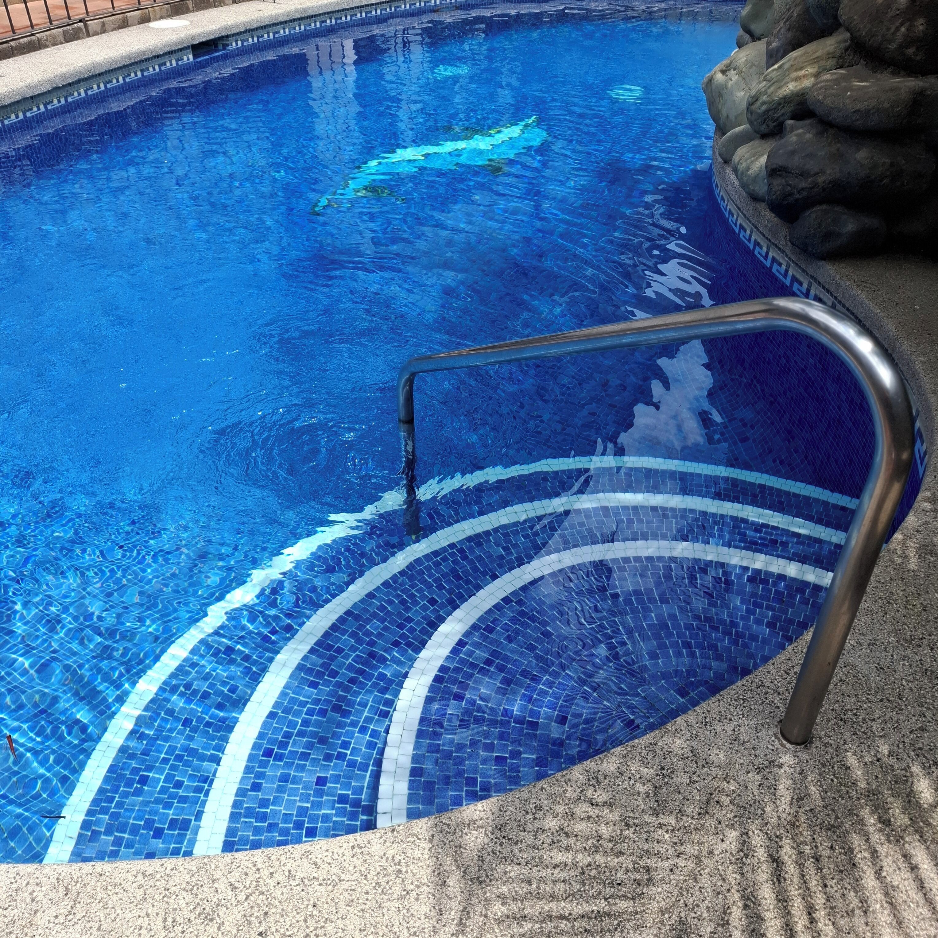 Une piscine à l’eau d’un bleu limpide, avec un escalier en métal et un bord carrelé.