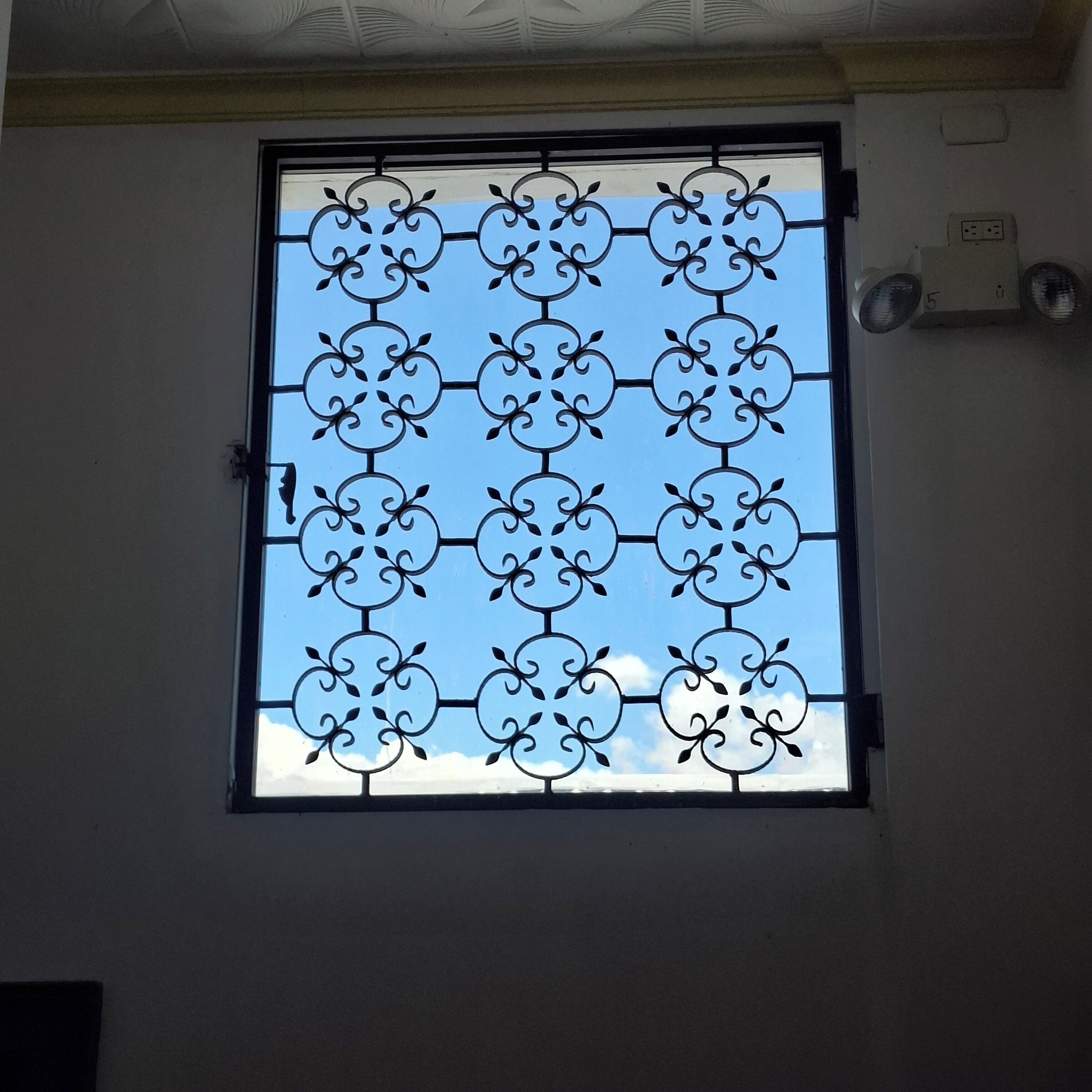 A window with a decorative metal grille and a clear blue sky view.