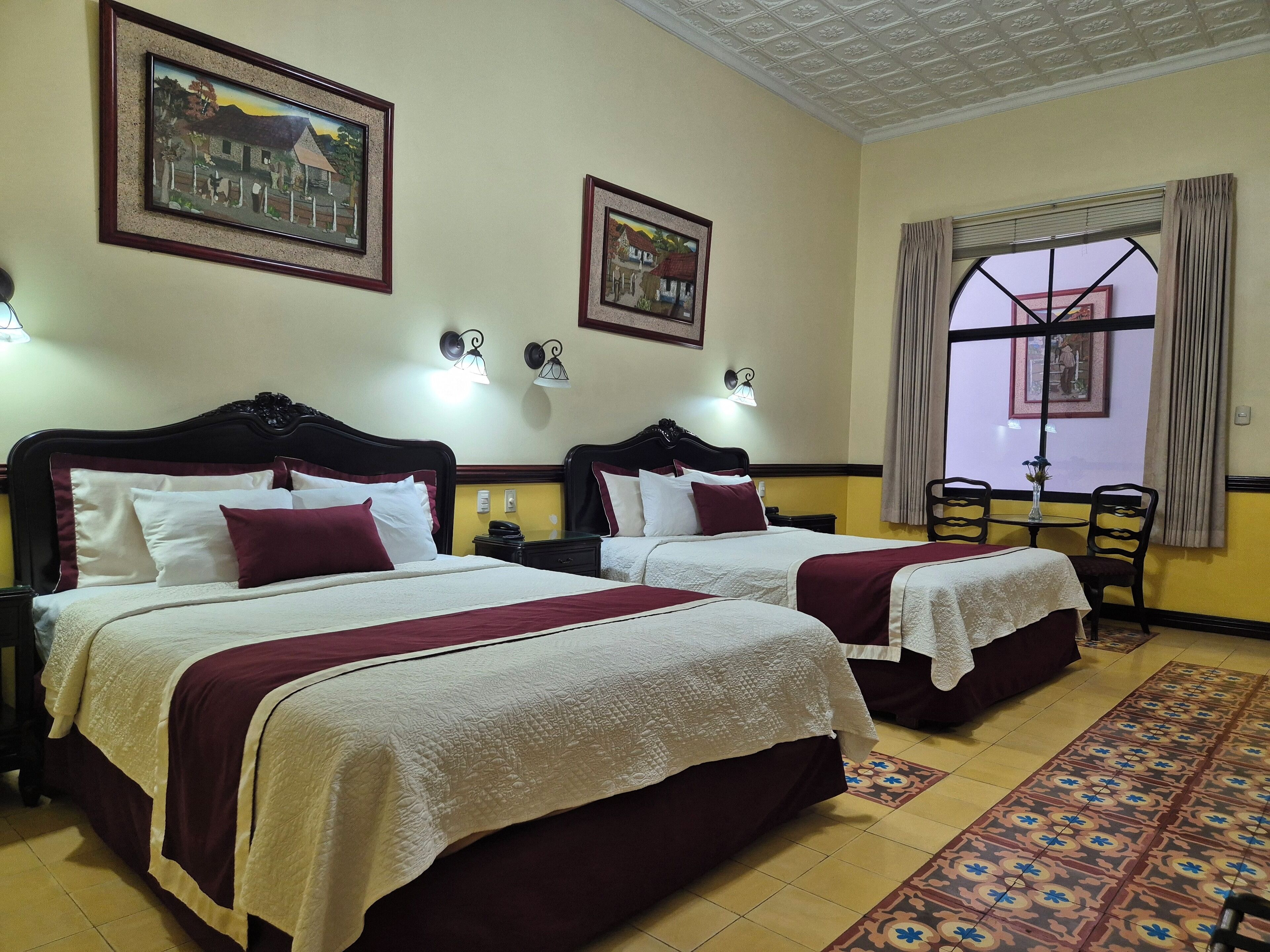 A hotel room with two beds, a patterned rug, and framed pictures on the walls.