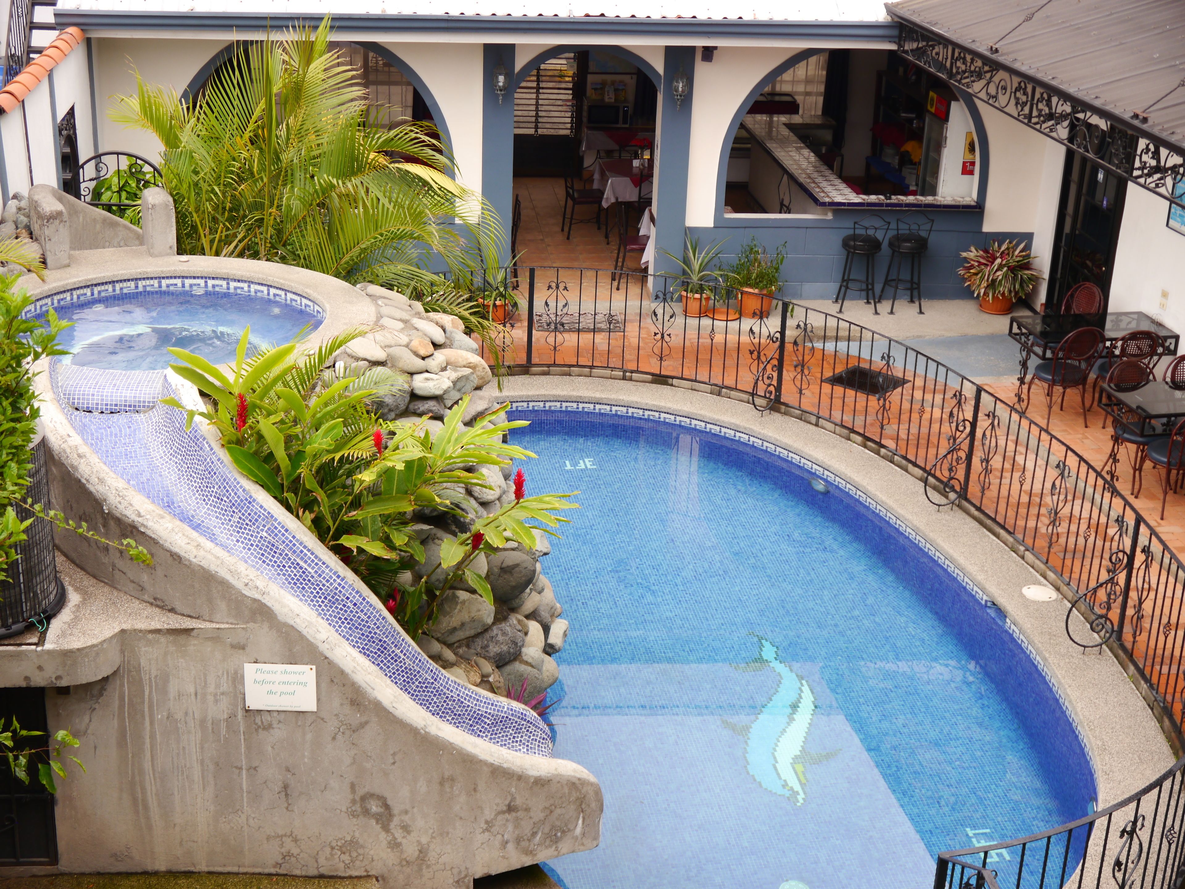 Una piscina con borde de azulejos, rodeada de un muro de piedra y plantas en macetas.