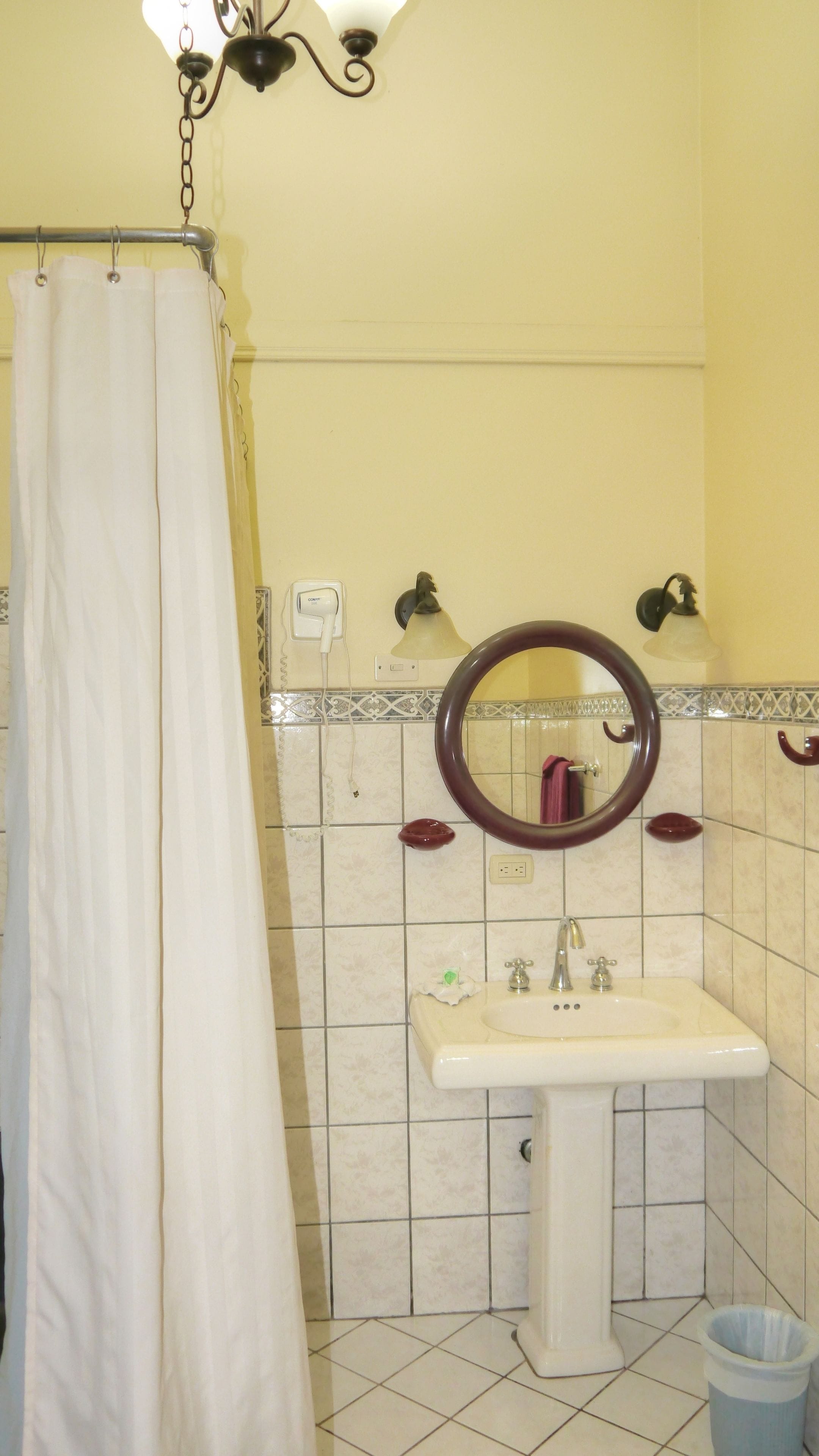 Une salle de bain avec un rideau de douche, un lavabo avec un miroir et une poubelle.