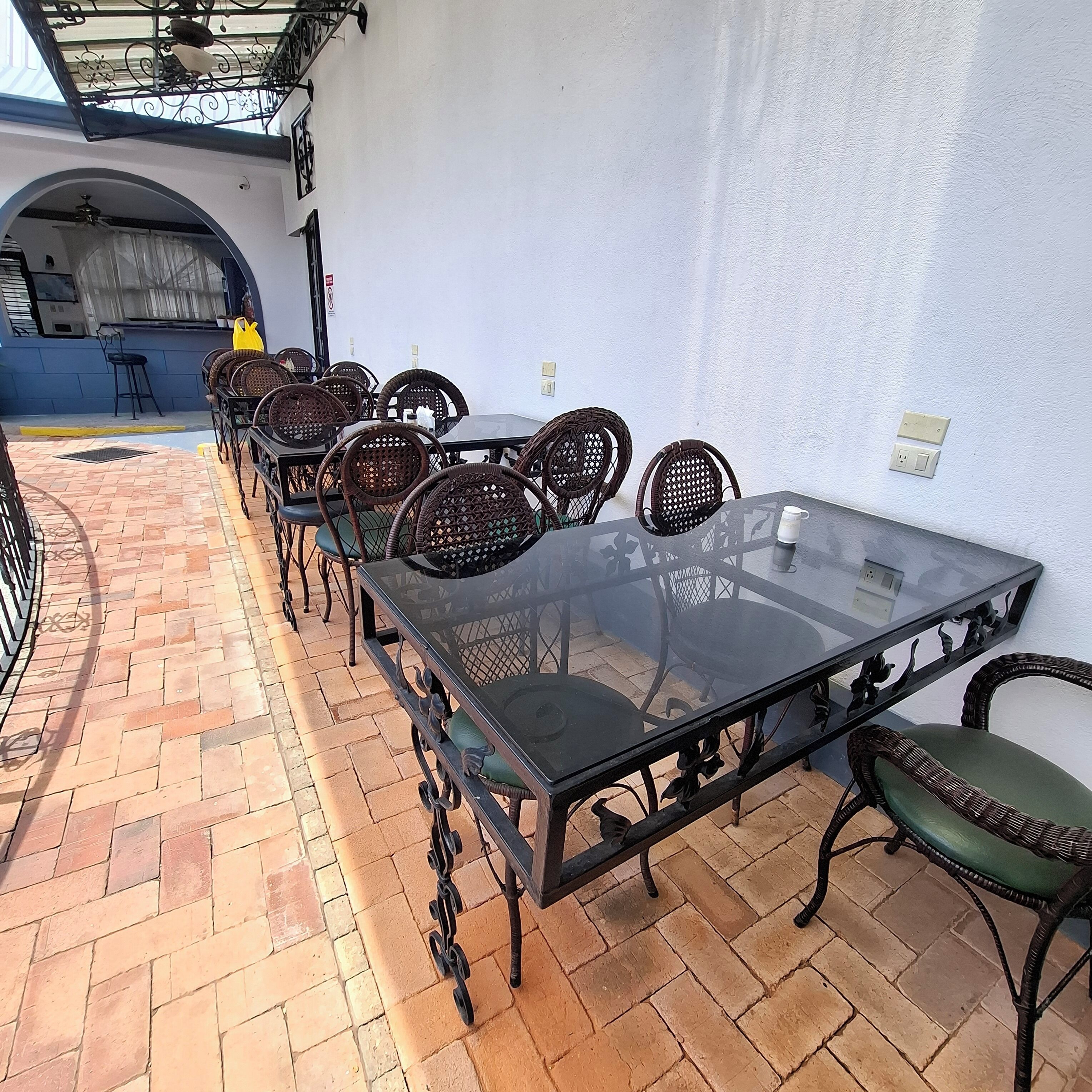 A patio with a glass-top table surrounded by wicker chairs, a blue wall, and a brick floor.
