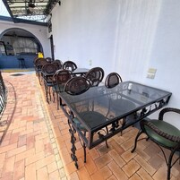 A patio with a glass-top table surrounded by wicker chairs, a blue wall, and a brick floor.