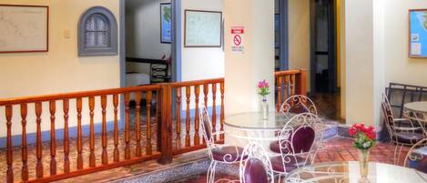 A room with a tiled floor, a round table with chairs, a ceiling fan, and a staircase with a wooden railing.