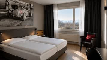 Habitación de hotel con una cama grande, un escritorio, una silla, una ventana con vistas y un cartel de un coche de carreras en la pared.
