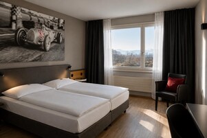 Habitación de hotel con una cama grande, un escritorio, una silla, una ventana con vistas y un cartel de un coche de carreras en la pared.