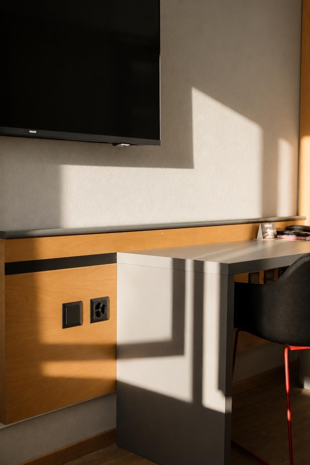 Ein modernes Zimmer mit einem wandmontierten Flachbildfernseher, einem Holztisch mit Stuhl und einem kleinen Tisch mit Tasse und Buch.