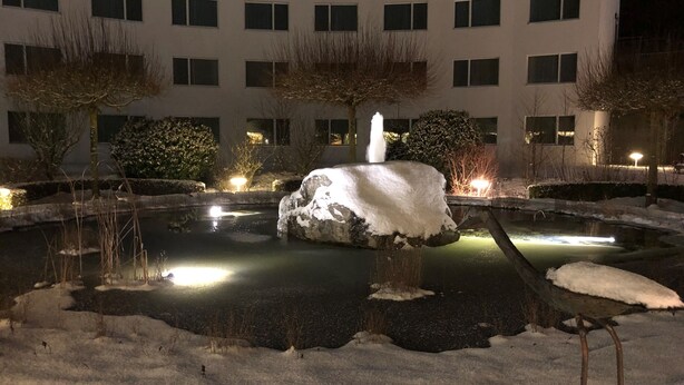 A snow-covered courtyard with a central fountain, surrounded by buildings with multiple windows. - Hotel Grauholz (Ittigen)