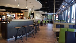 A modern cafe with a curved counter, bar stools, and green and blue seating. - Hotel Grauholz (Ittigen)