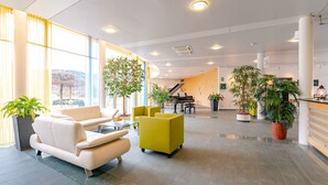 A spacious lobby with a piano, seating areas, and potted plants. - Hotel Grauholz (Ittigen)