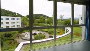 A view from a hotel room with large windows overlooking a landscaped garden, a circular water feature, and a building with a yellow slide. - Hotel Grauholz (Ittigen)