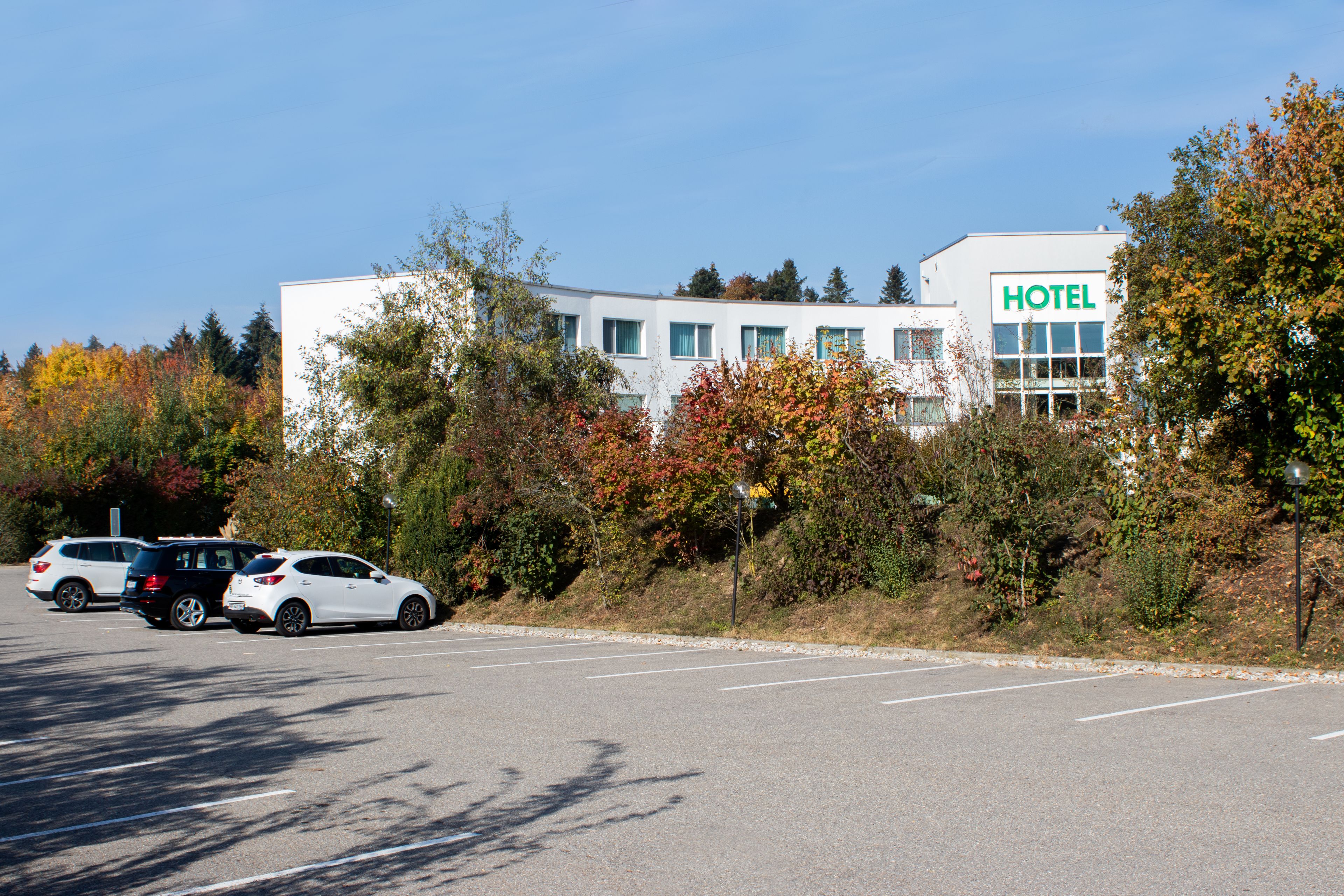 Ein Hotelgebäude im modernen Design, ein Parkplatz und Herbstlaub.