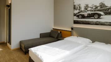 Quarto de hotel com cama, sofá, mesa de cabeceira e luminária na parede.