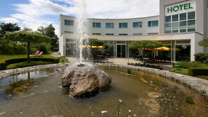 A hotel with a fountain in the courtyard, outdoor seating, and a well-maintained garden. - Hotel Grauholz (Ittigen)