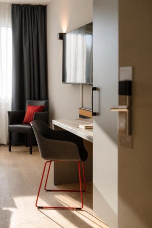 Una habitación moderna con escritorio, una silla, televisor y ventana con cortinas.