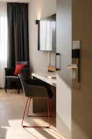A modern room with a desk, a chair, a television, and a window with curtains.