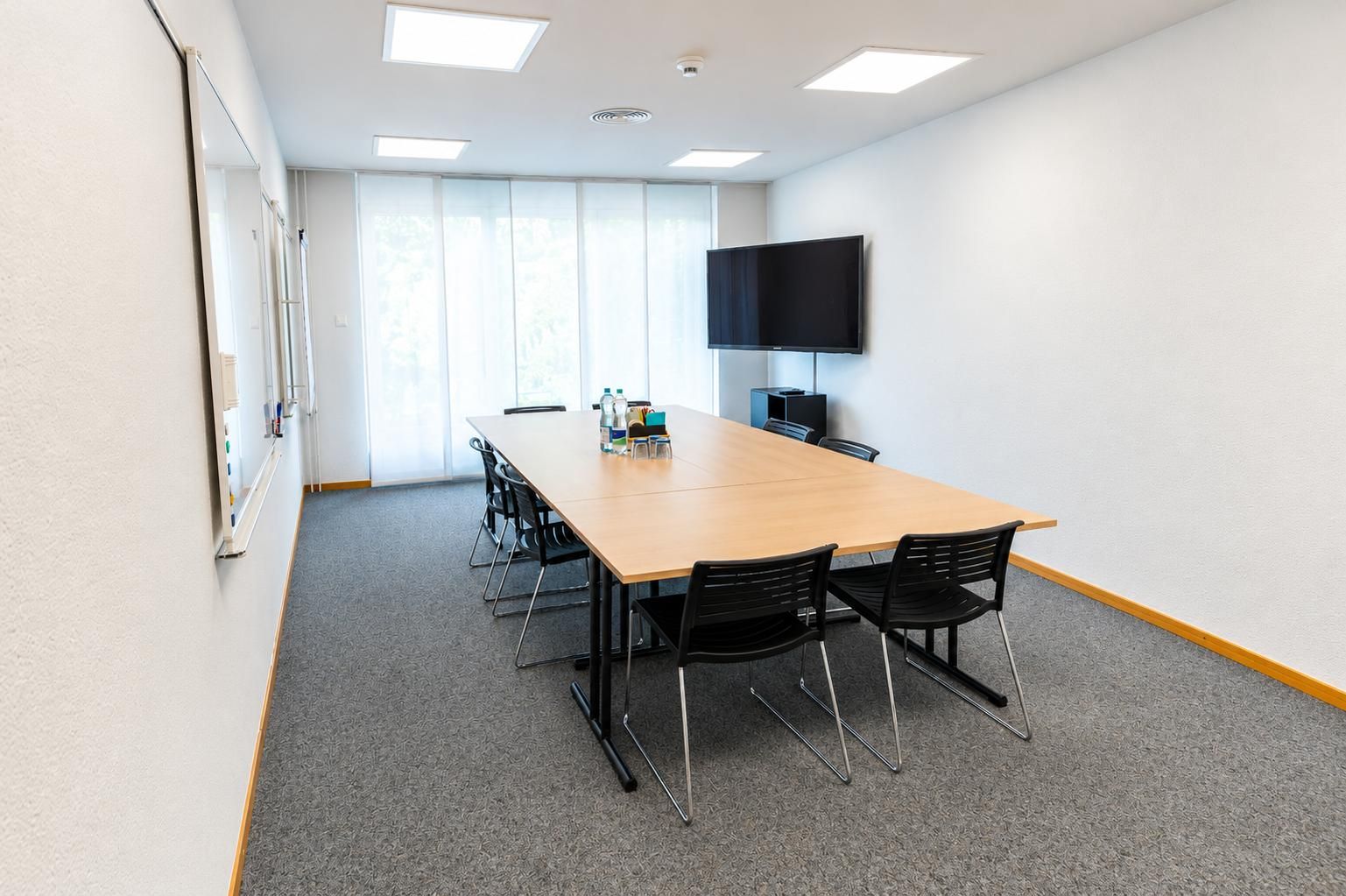 Une salle de conférence équipée d’une longue table, de chaises, d’un téléviseur à écran plat et d’un tableau blanc.