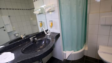Une salle de bain avec un lavabo noir, deux distributeurs de savon, des toilettes et un rideau de douche.