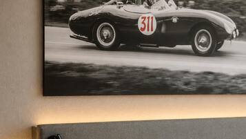 Une chambre à coucher comprenant un lit, une tête de lit, une table de chevet et un tableau représentant une voiture ancienne, accroché au mur.