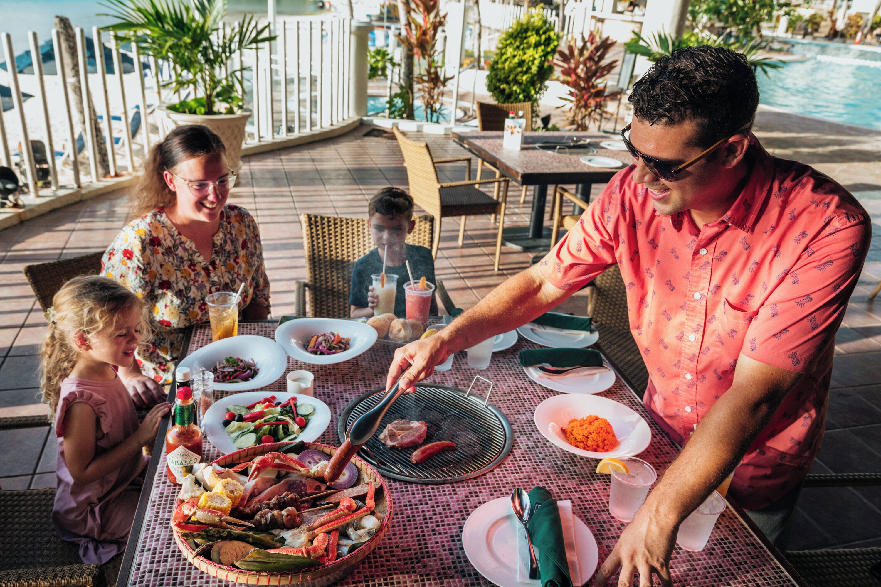Una mesa de comedor con varios platos, una parrilla y una piscina al fondo.