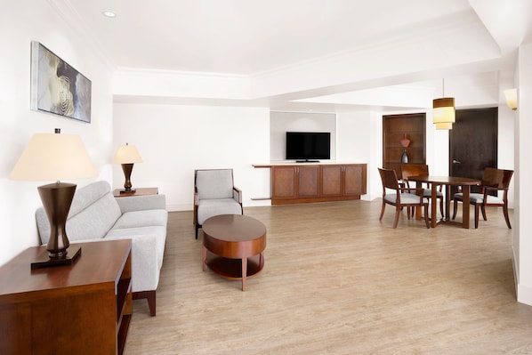 A spacious living area with a sofa, armchair, round coffee table, and dining table with chairs. A flat-screen TV is mounted above a wooden cabinet. - The Westin Resort Guam (Tamuning)