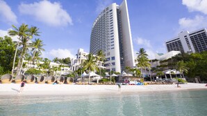 A beachfront hotel with a modern design, featuring a curved facade, multiple balconies, and a pool area.