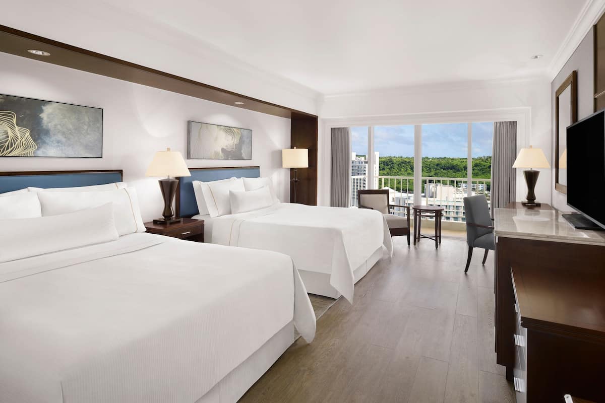 A hotel room with two beds, a desk, a chair, and a TV.